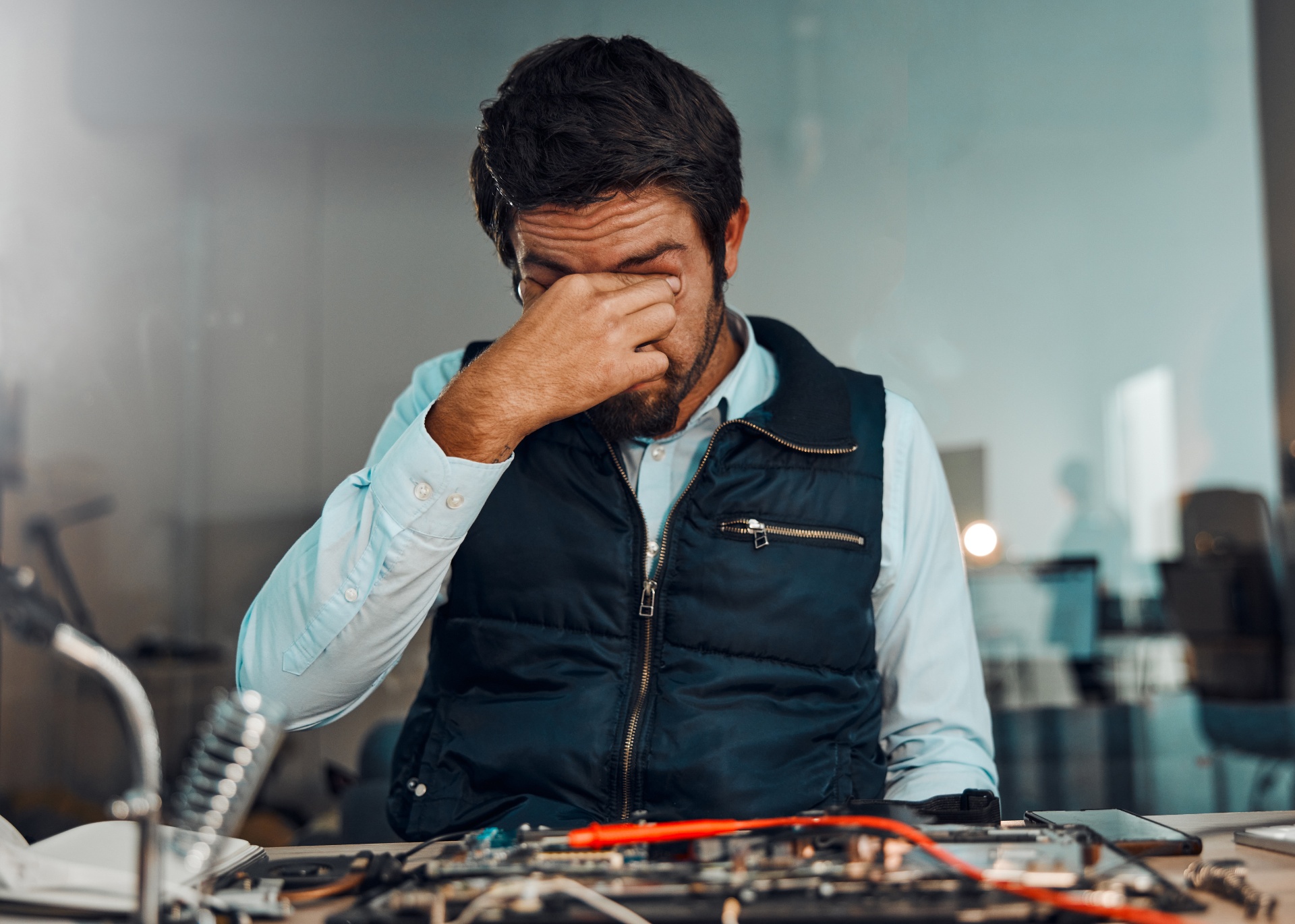Técnico frustrado com a mão no rosto em oficina de eletrônica